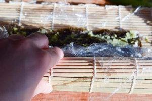 Maki Sushi mit Lachs & Avocado: aufrollen des Nori Blattes mit der Matte
